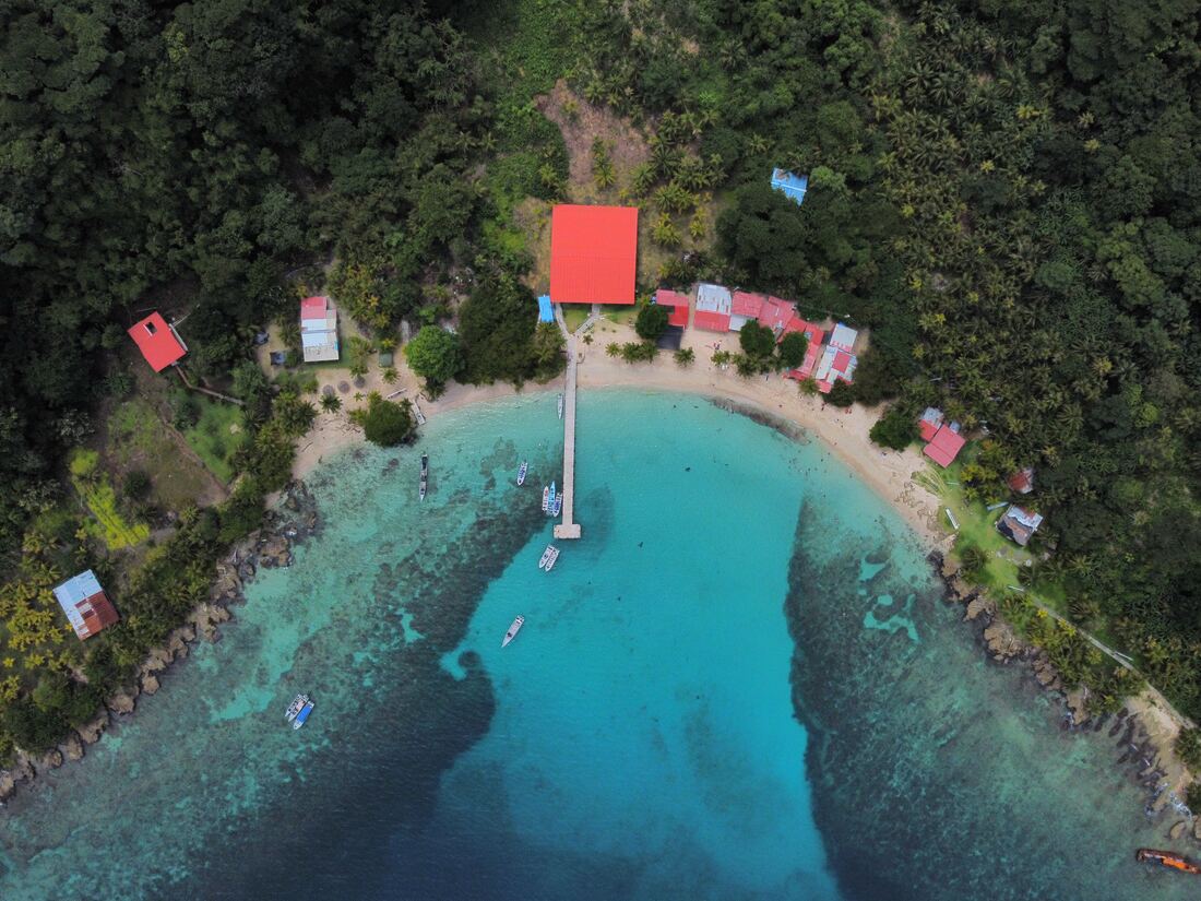 Vista aérea de cala turquesa con muelle y techos rojos