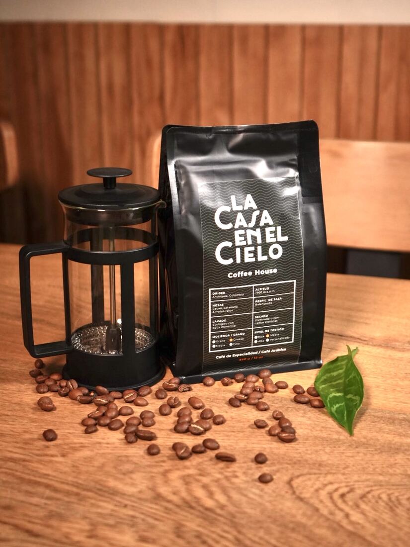 Bolsa de café de especialidad junto a prensa francesa y granos