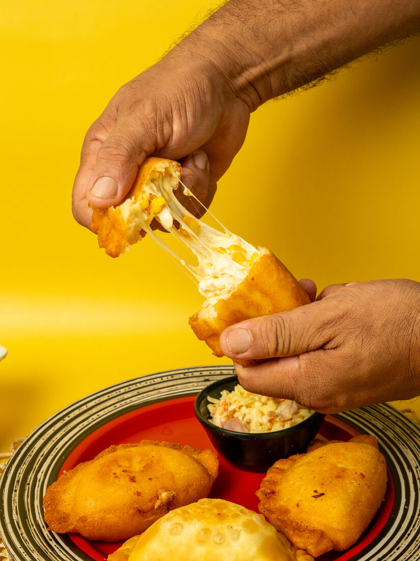 Manos partiendo una empanada con queso derretido