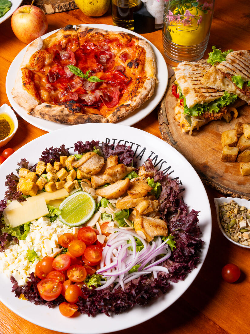 Mesa servida con pizza, ensalada y sándwich